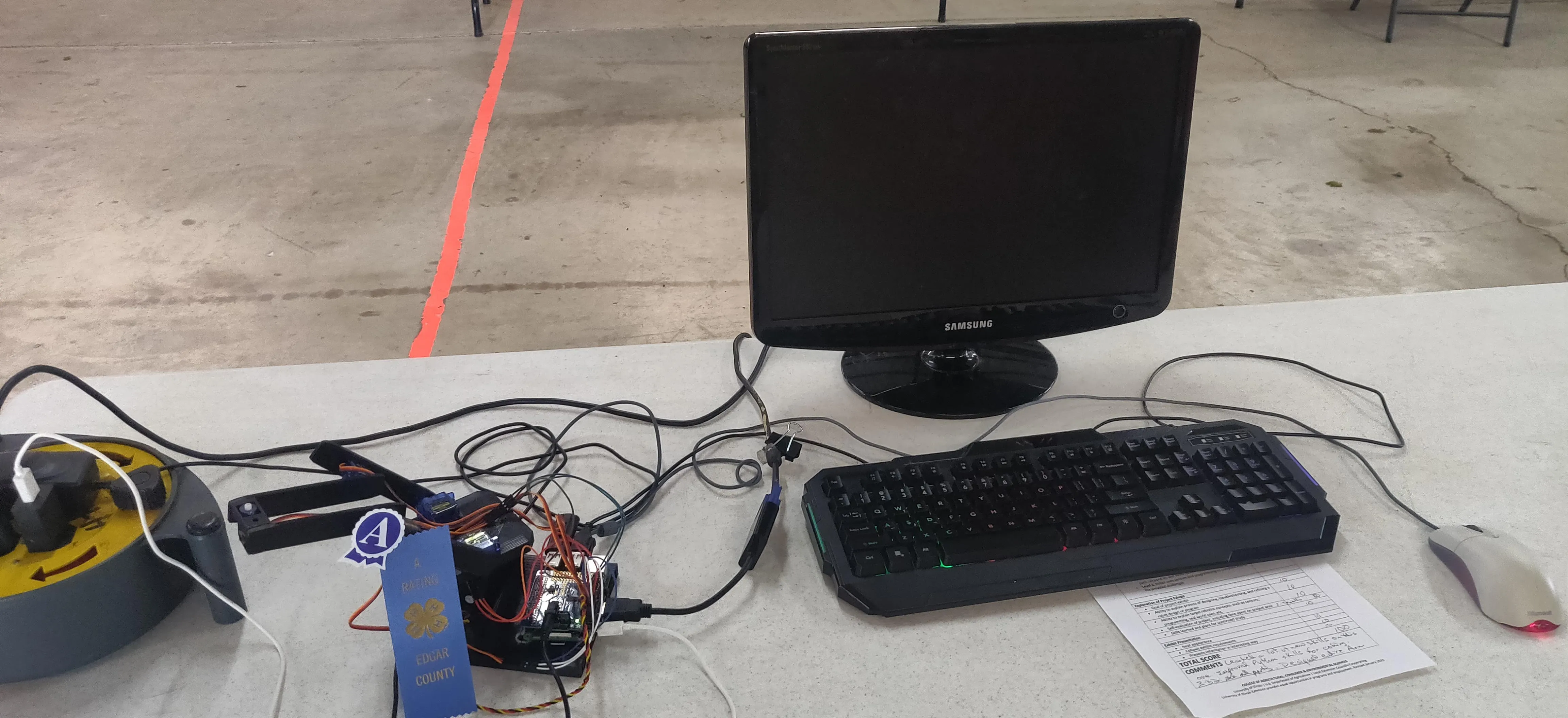 The robotic arm on the competition table with its control station and first-place ribbon